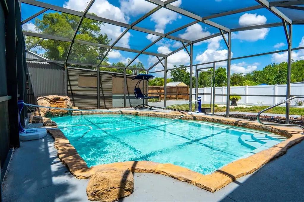 A screened-in swimming pool with a rock waterfall feature and a volleyball net — 1118 OVERDALE STREET, ORLANDO, FL