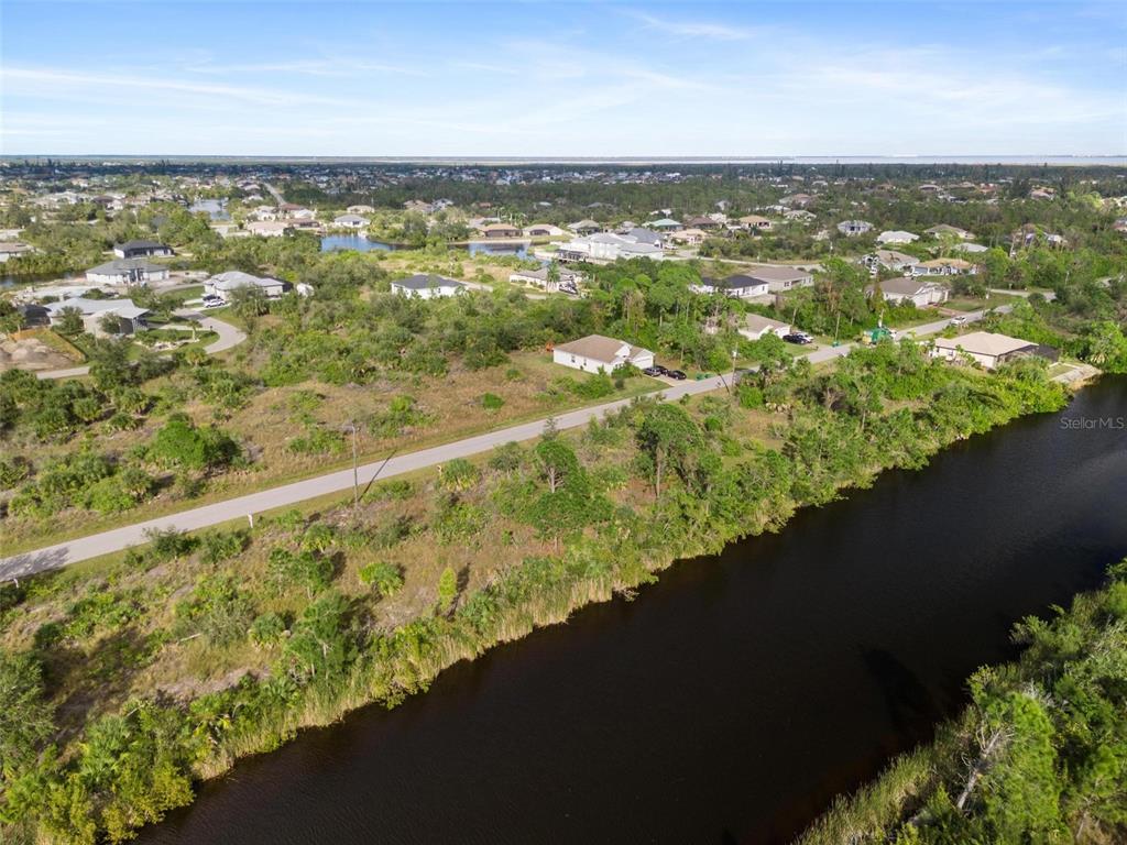 An aerial view shows a residential neighborhood with a canal, paved road, and scattered houses — 15109 AMSTERDAM AVENUE, PORT CHARLOTTE, FL