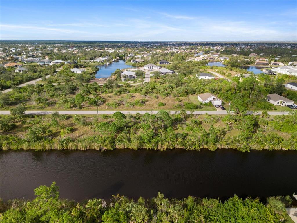 An aerial view shows a canal in the foreground with houses and vegetation beyond — 15109 AMSTERDAM AVENUE, PORT CHARLOTTE, FL