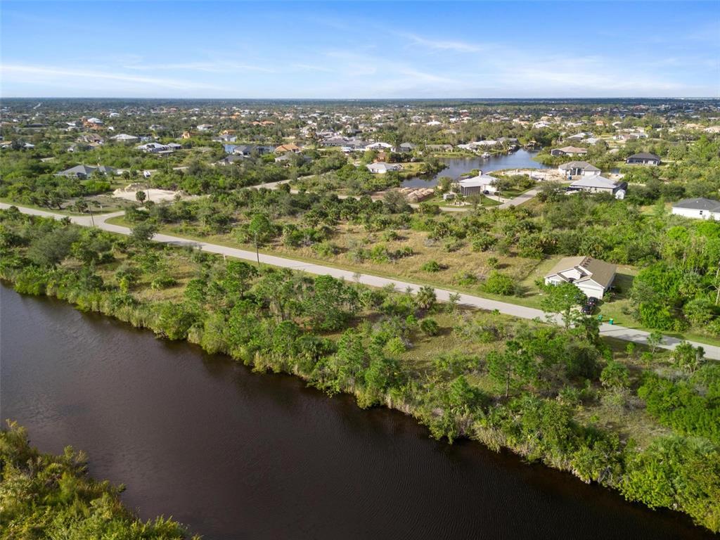 An aerial view shows a canal bordering a grassy lot with a house and road — 15109 AMSTERDAM AVENUE, PORT CHARLOTTE, FL