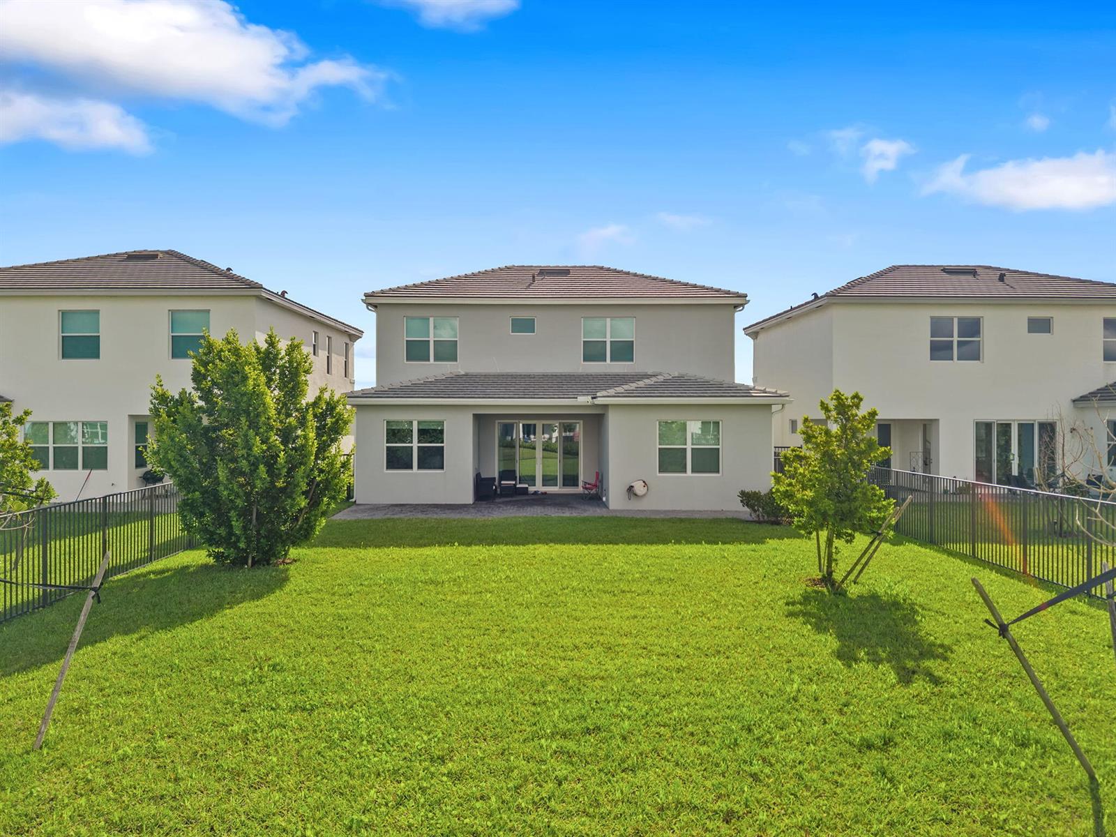 The rear exterior of a two-story house features a patio, lawn, and metal fencing — 5455 Empire Drive, Westlake FL 33470, WESTLAKE, FL