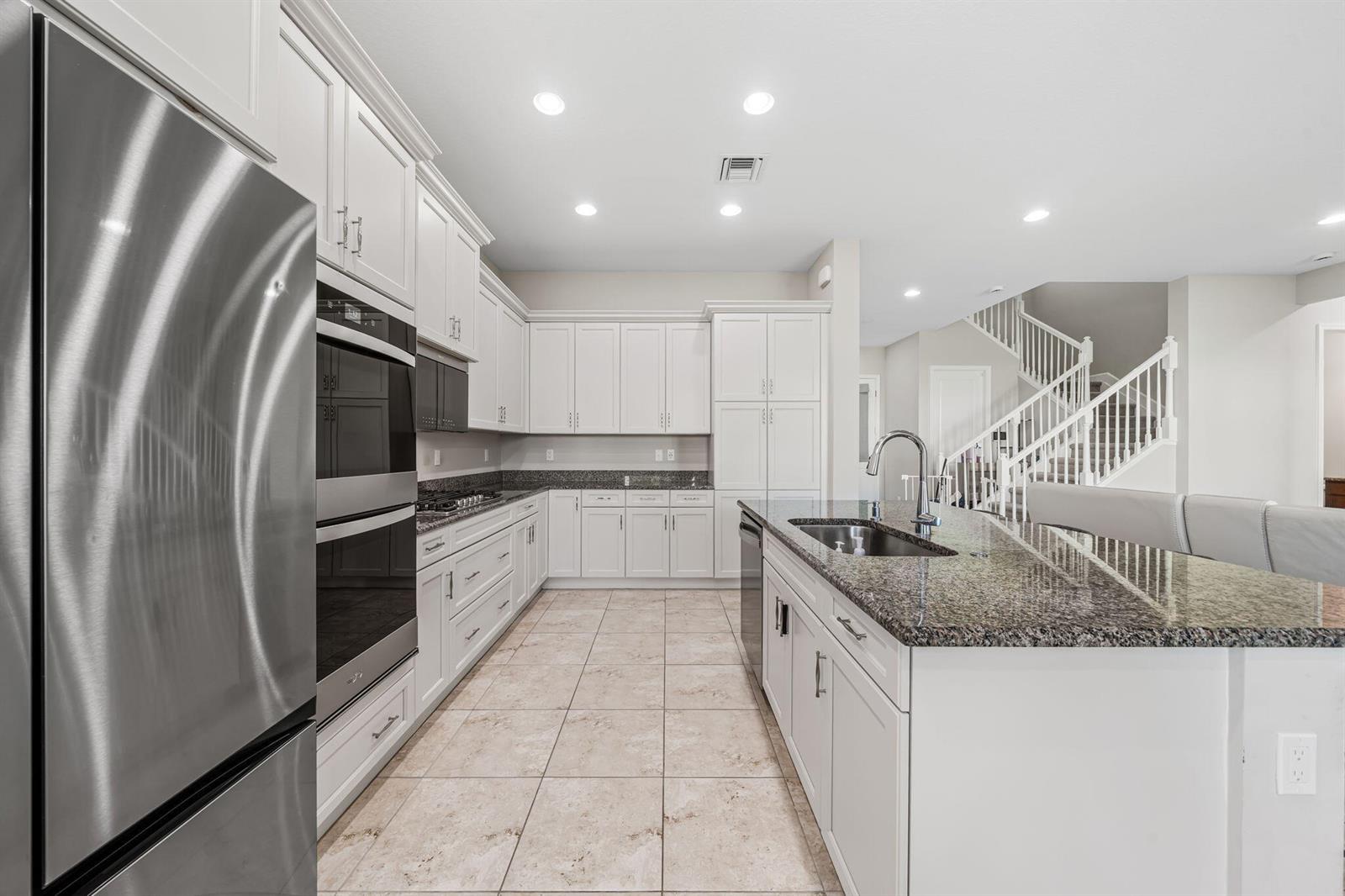 A modern kitchen features white cabinetry, granite countertops, stainless steel appliances, and tile flooring — 5455 Empire Drive, Westlake FL 33470, WESTLAKE, FL