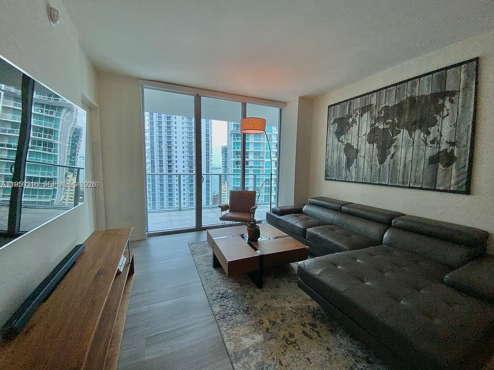 A modern living room features a dark leather sectional, wood coffee table, and floor-to-ceiling windows — 1100 S Miami Ave # 2811, Miami FL 33130, MIAMI, FL