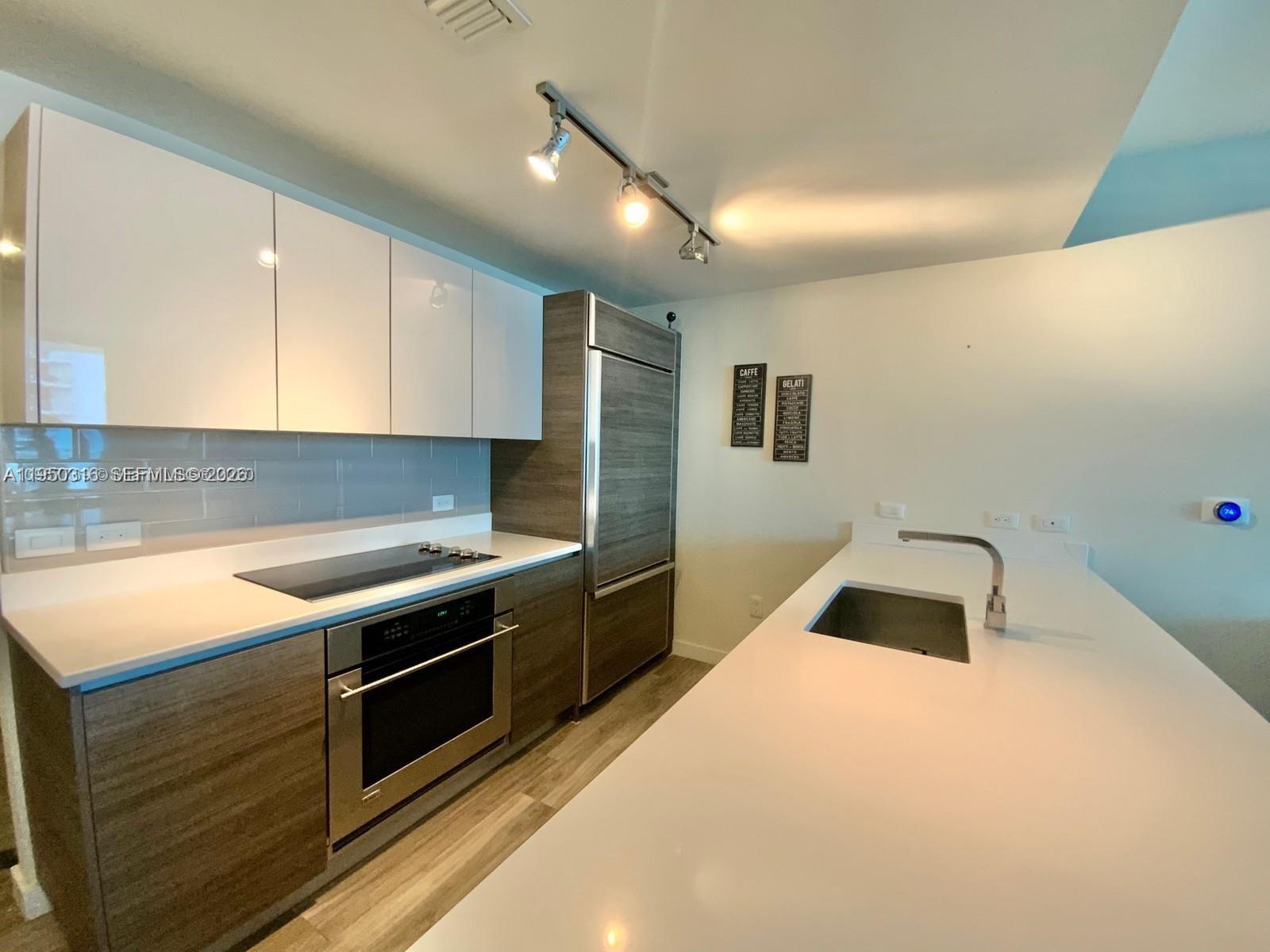 A modern kitchen features white cabinets, wood-grain lower cabinets, stainless steel appliances, and white countertops — 1100 S Miami Ave # 2811, Miami FL 33130, MIAMI, FL