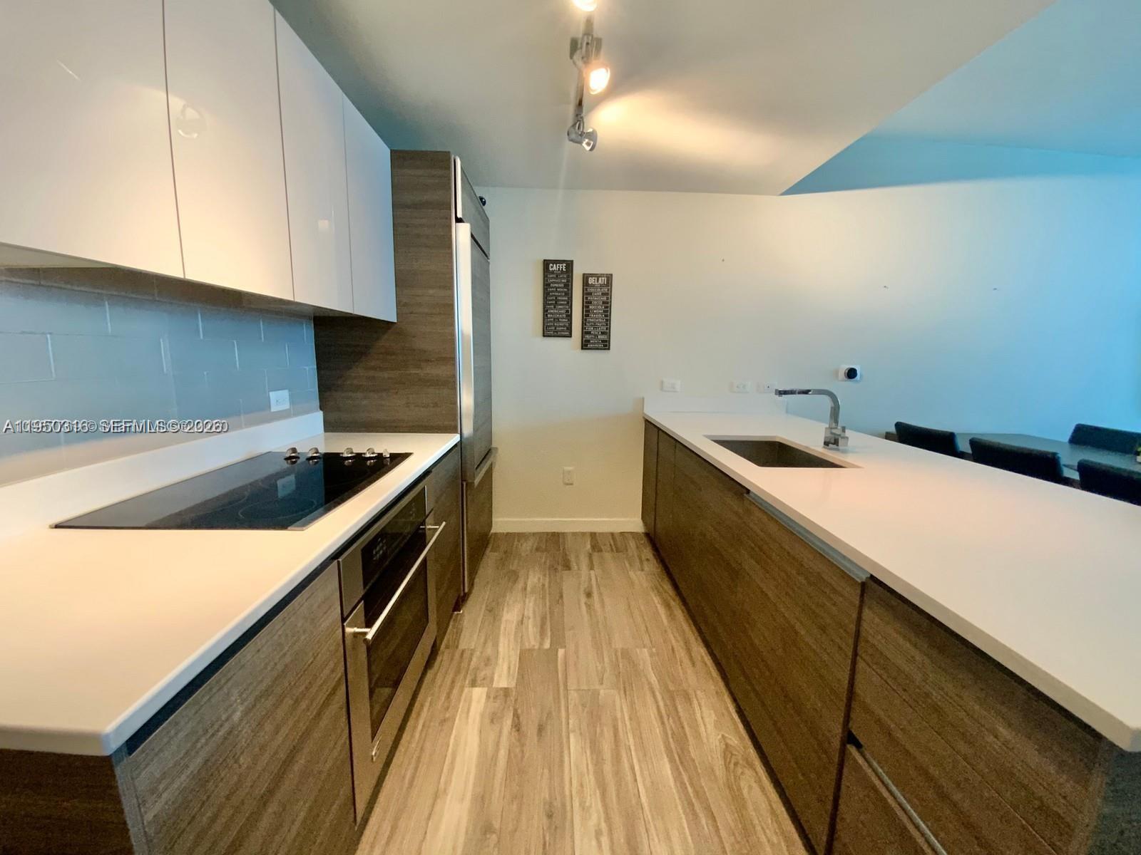 A modern galley kitchen features white upper cabinets, wood-grain lower cabinets, and white countertops — 1100 S Miami Ave # 2811, Miami FL 33130, MIAMI, FL