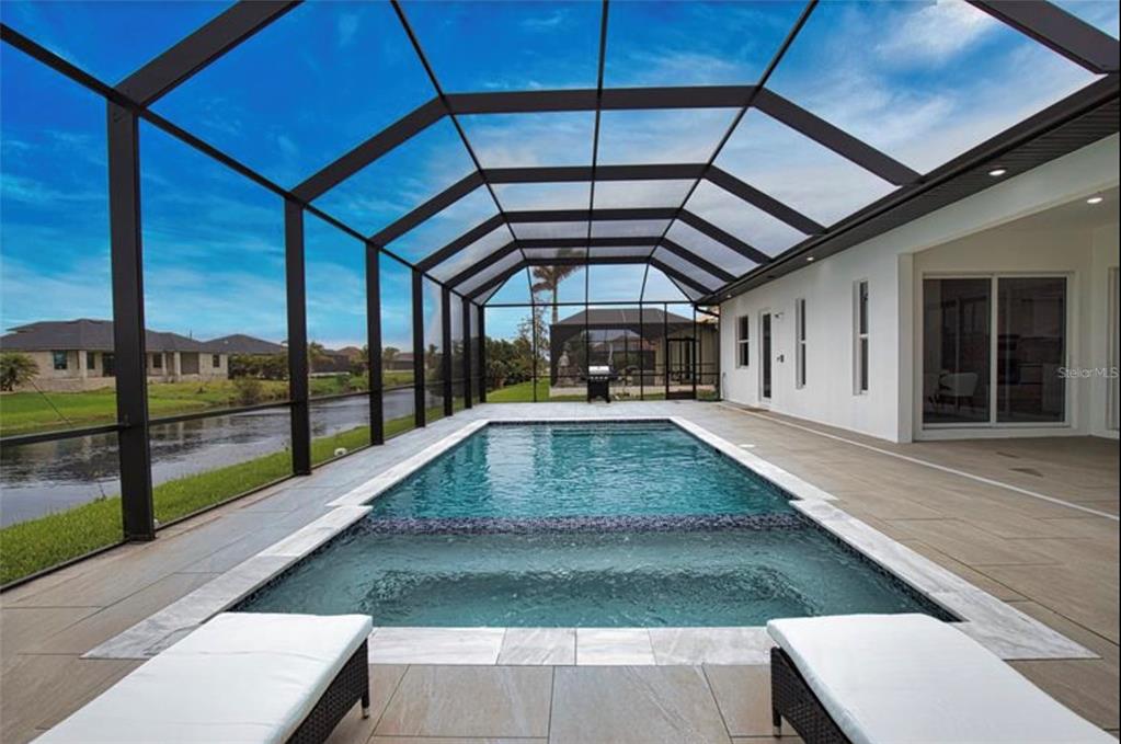 A screened-in pool and spa area with tile decking overlooking a canal and neighboring houses — 230 W PINE VALLEY LANE, ROTONDA WEST, FL