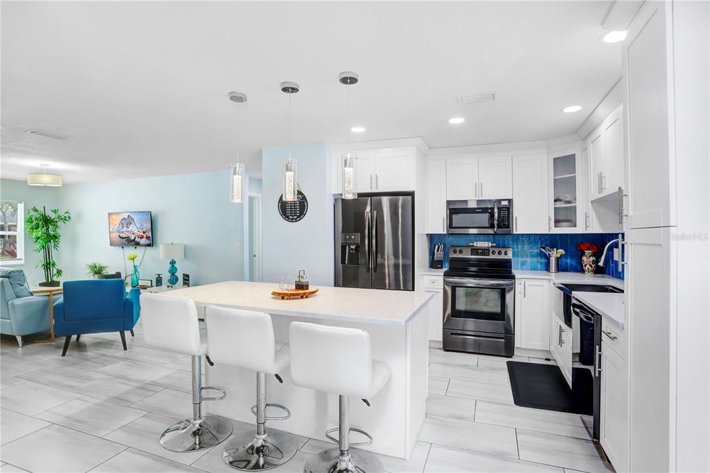A modern kitchen features white cabinetry, stainless steel appliances, a center island, and blue tile — 12819 129TH TERRACE, LARGO, FL