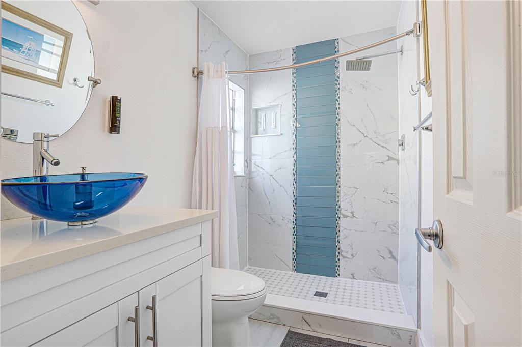 A bathroom features a blue glass vessel sink, white vanity, and a tiled walk-in shower — 12819 129TH TERRACE, LARGO, FL