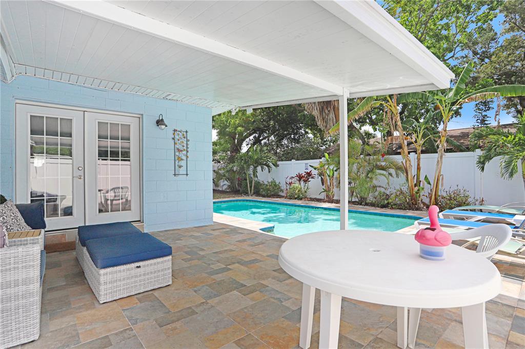 A covered patio with stone tile flooring overlooks a backyard swimming pool and tropical landscaping — 12819 129TH TERRACE, LARGO, FL