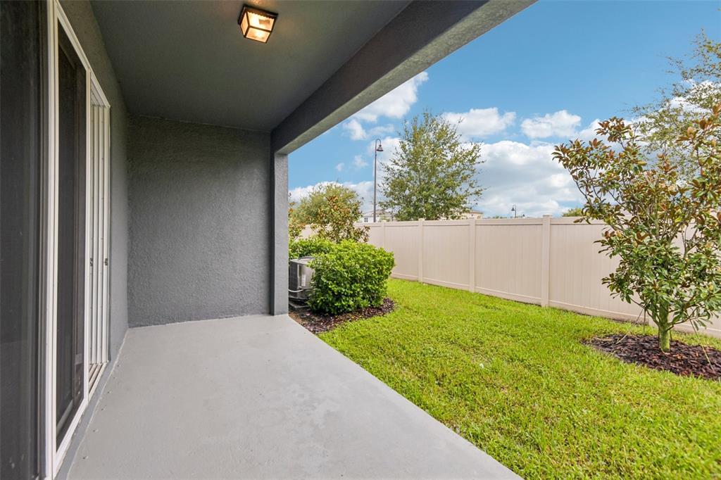 A covered concrete patio overlooks a grassy backyard enclosed by a tan vinyl fence — 2685 SUNCOAST BLEND DRIVE, ODESSA, FL