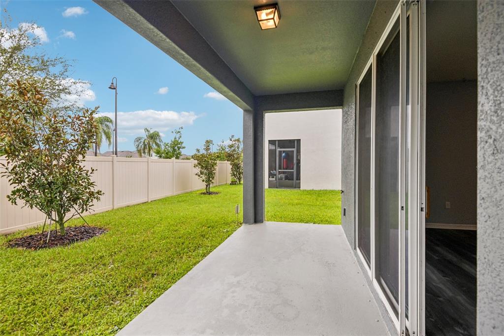A covered concrete patio overlooks a grassy backyard enclosed by a tan vinyl fence — 2685 SUNCOAST BLEND DRIVE, ODESSA, FL