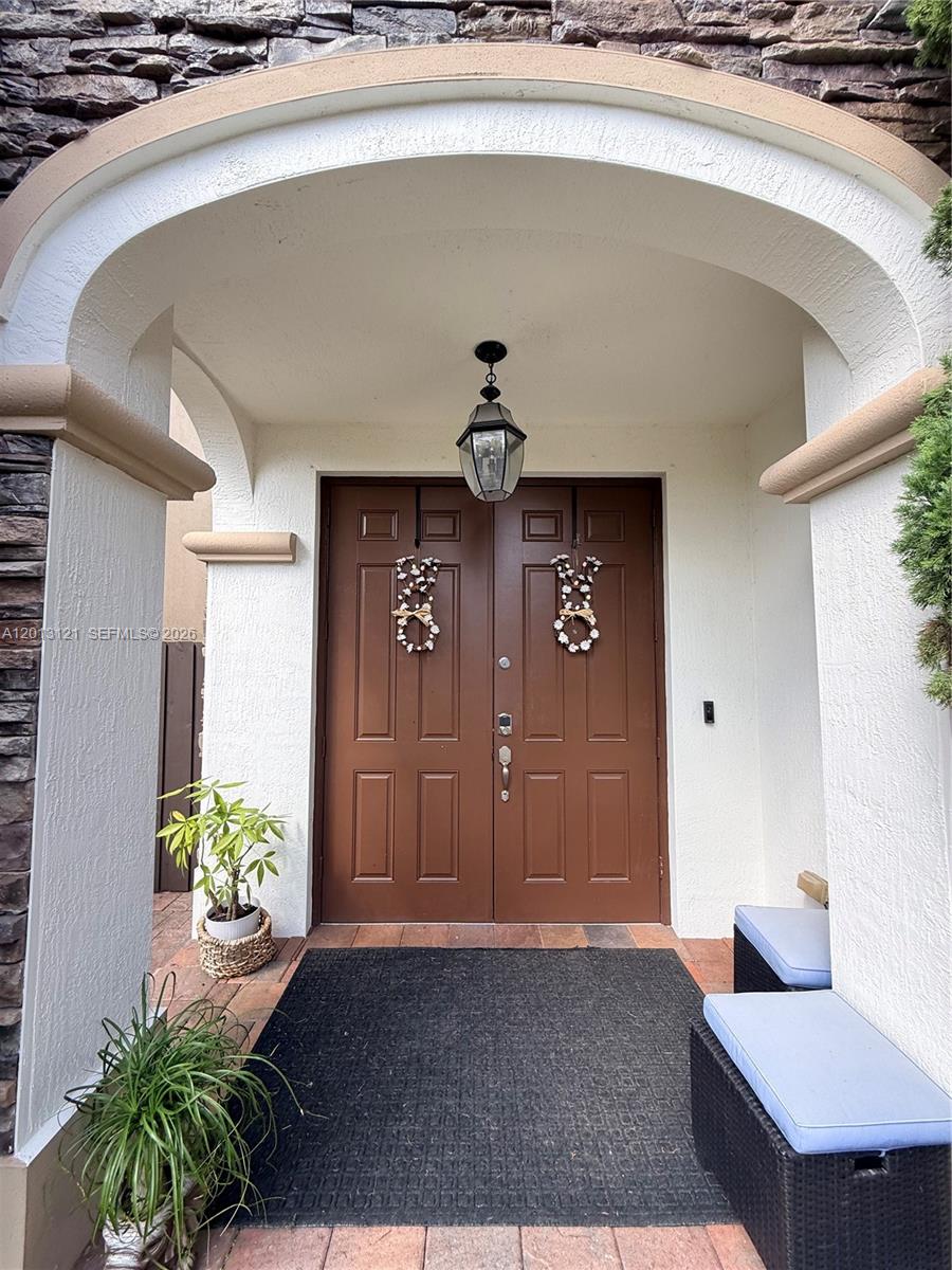 A covered entryway features double brown doors, a hanging lantern, and two outdoor benches — 8640 NW 101st Pl, Doral FL 33178, DORAL, FL
