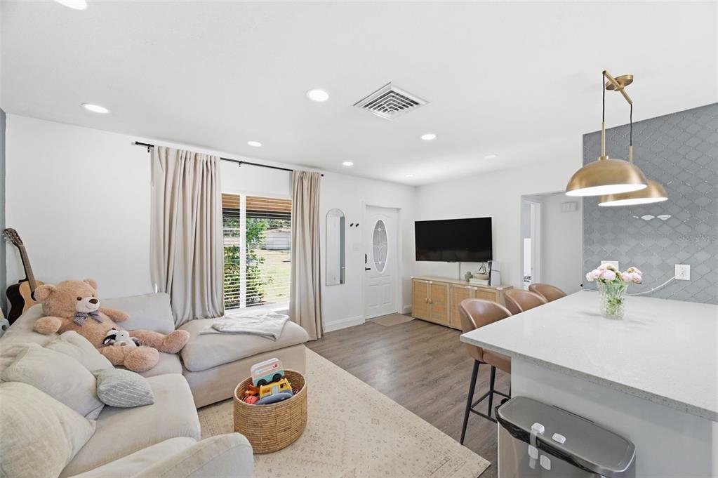 A living room and kitchen area with light-colored furniture, wood-look flooring, and a breakfast bar — 2150 76TH STREET N, ST PETERSBURG, FL