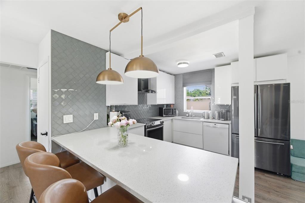 A modern kitchen features white cabinetry, a quartz island, and a gray tiled accent wall — 2150 76TH STREET N, ST PETERSBURG, FL