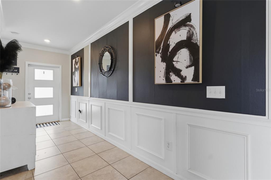 A hallway features white wainscoting, black accent walls, framed abstract art, and tiled flooring — 14801 BOULDER PASS PLACE, WIMAUMA, FL