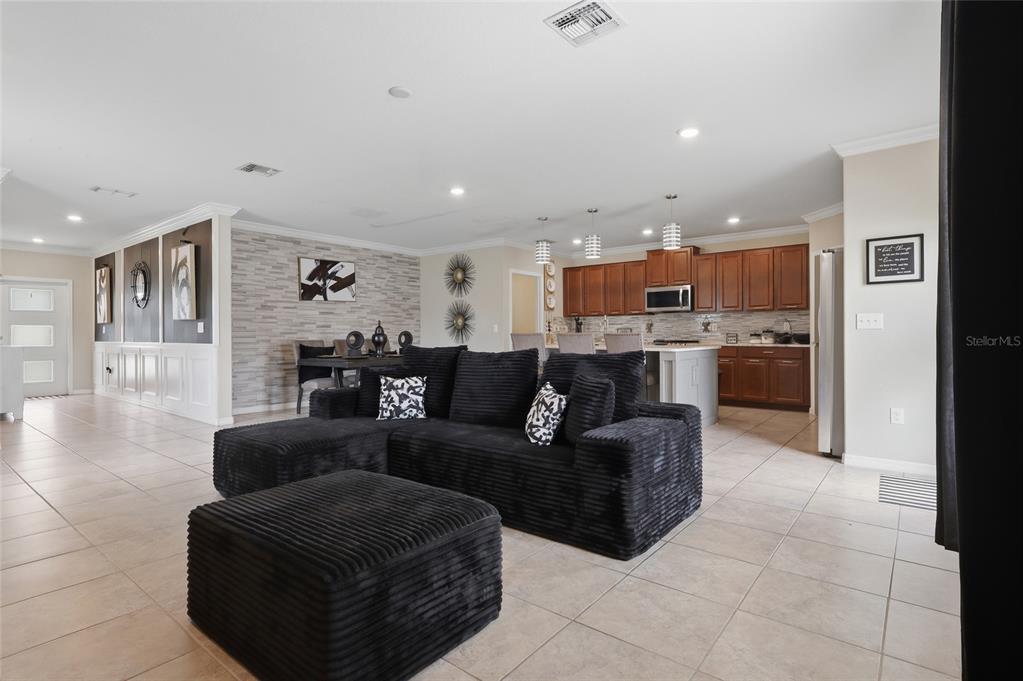 An open-concept living room and kitchen featuring tile floors, a black sectional, and wood cabinetry — 14801 BOULDER PASS PLACE, WIMAUMA, FL