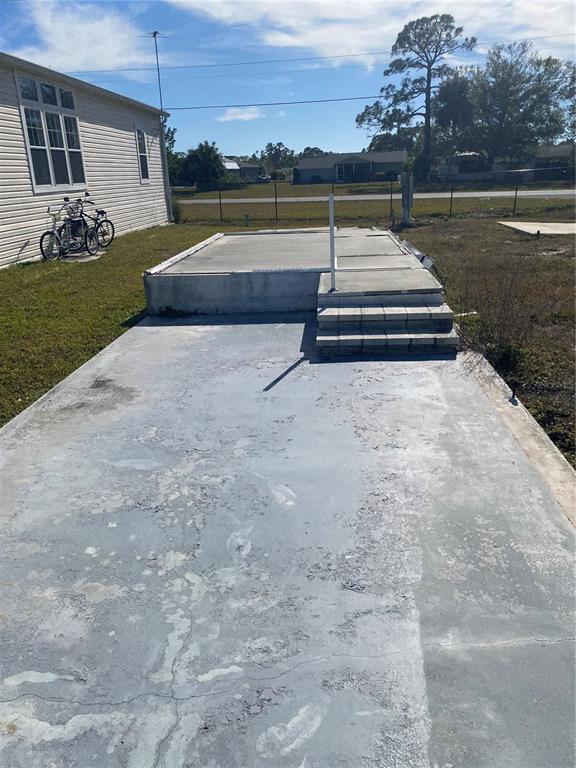 A concrete patio with steps sits adjacent to a house exterior and a grassy yard — 6684 ACACIA COURT, NORTH PORT, FL