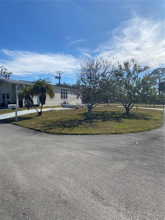 A light-colored mobile home sits behind a grassy yard with several trees and a driveway — 6684 ACACIA COURT, NORTH PORT, FL