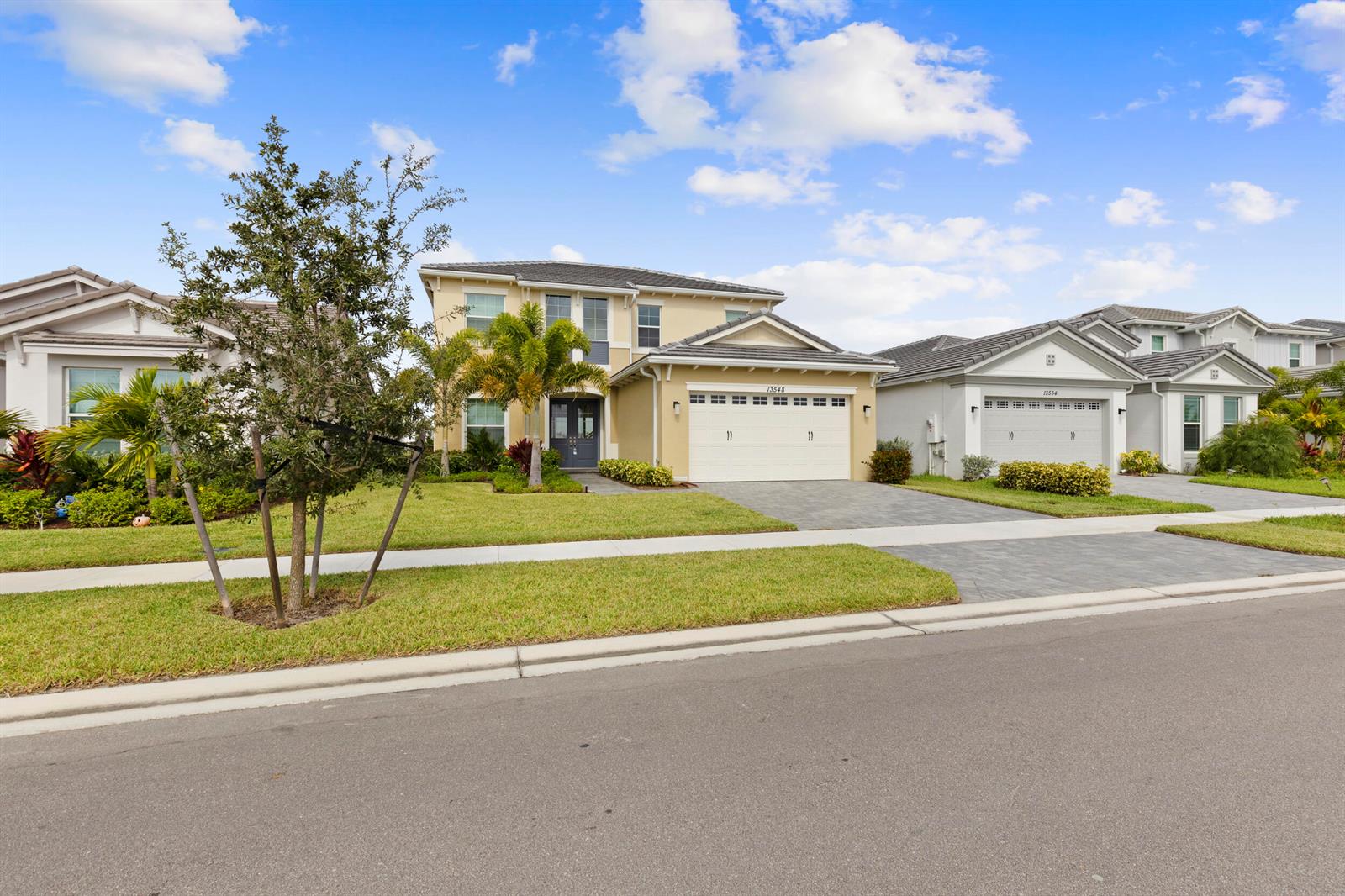A two-story suburban house with a beige exterior, a white garage, and a landscaped lawn — 13548 Spruce Pine Drive, Westlake FL 33470, WESTLAKE, FL
