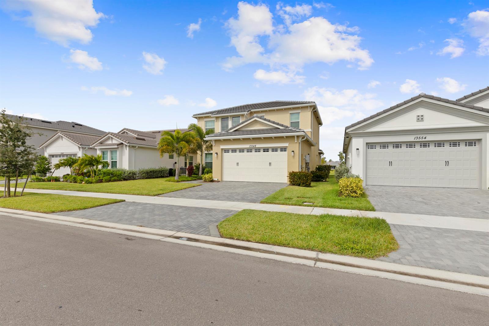 A two-story tan house with a paved driveway sits between two single-story homes — 13548 Spruce Pine Drive, Westlake FL 33470, WESTLAKE, FL