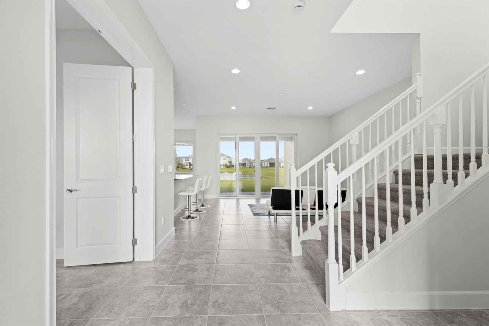 A bright entryway features gray tile flooring, a carpeted staircase, and a view of a pond — 13548 Spruce Pine Drive, Westlake FL 33470, WESTLAKE, FL