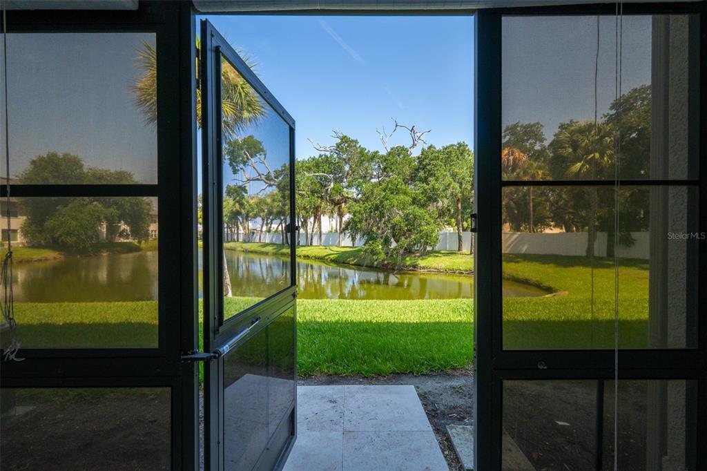 A view of a pond and trees seen through an open screen door — 150 PORTSIDE AVENUE UNIT 103, CAPE CANAVERAL, FL