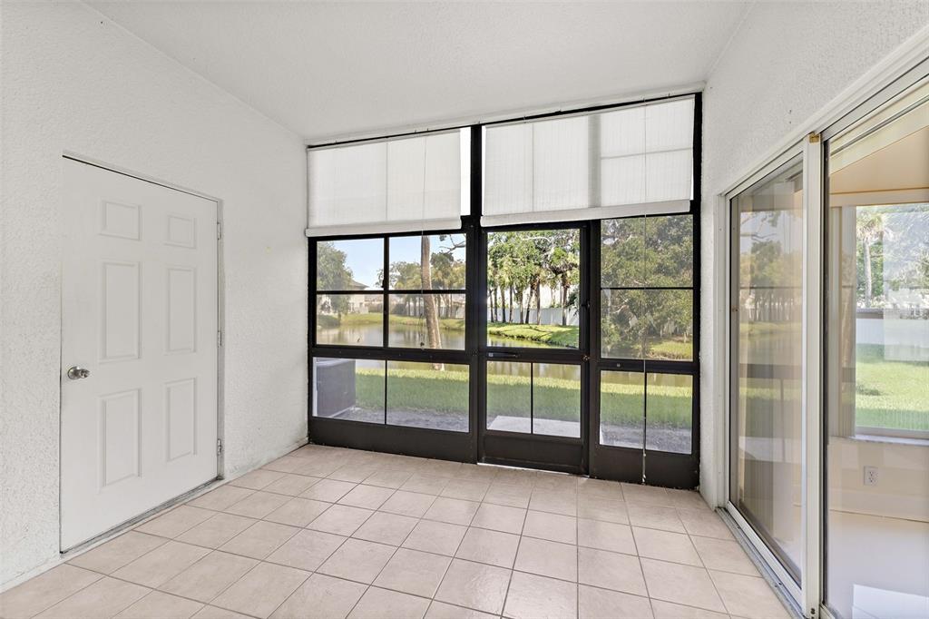 A sunroom with white walls, tiled flooring, a white door, and large screened windows — 150 PORTSIDE AVENUE UNIT 103, CAPE CANAVERAL, FL