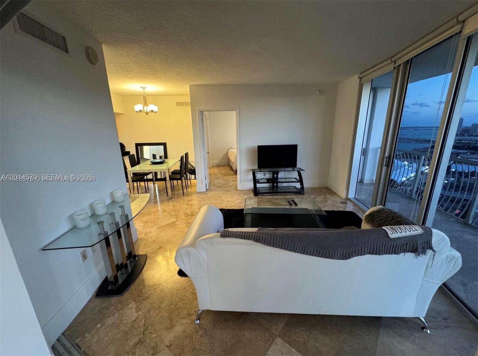 A living room with a white sofa, glass coffee table, and dining area with balcony views — 1750 N Bayshore Dr # 3114, Miami FL 33132, MIAMI, FL