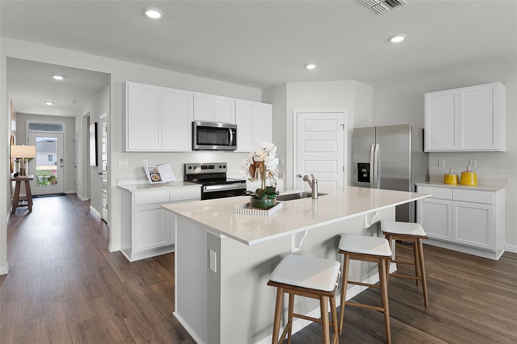 A modern kitchen features white cabinets, a central island with bar seating, and stainless appliances — 3529 RODEN ROAD, HAINES CITY, FL