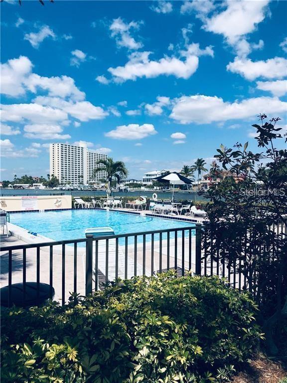 A swimming pool with lounge chairs sits near a body of water and tall buildings — 7405 BAY ISLAND DRIVE S UNIT 224, SOUTH PASADENA, FL