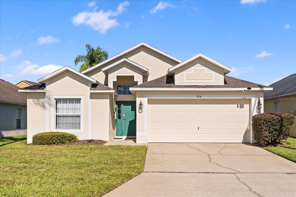A single-story house with a beige stucco exterior, a green front door, and a driveway — 316 TIVOLI CIRCLE, DAVENPORT, FL