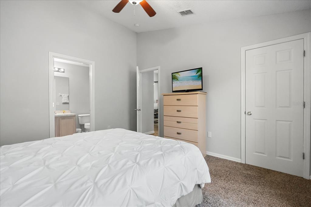A bedroom features a white bed, a light wood dresser with a television, and carpet — 316 TIVOLI CIRCLE, DAVENPORT, FL