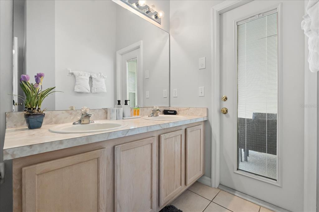 A bathroom features a double vanity with light wood cabinets, a marble-look countertop, and a door — 316 TIVOLI CIRCLE, DAVENPORT, FL