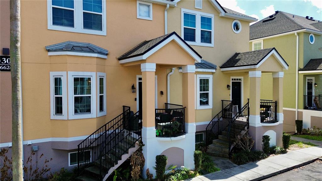 An exterior view of two adjacent townhouses with elevated porches, stairs, and beige siding — 6624 TIME SQUARE AVENUE UNIT 102, ORLANDO, FL