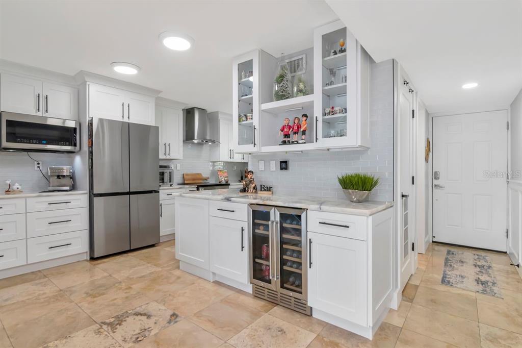 A modern white kitchen features stainless steel appliances, a wine cooler, and stone tile flooring — 2424 W TAMPA BAY BOULEVARD UNIT C105, TAMPA, FL