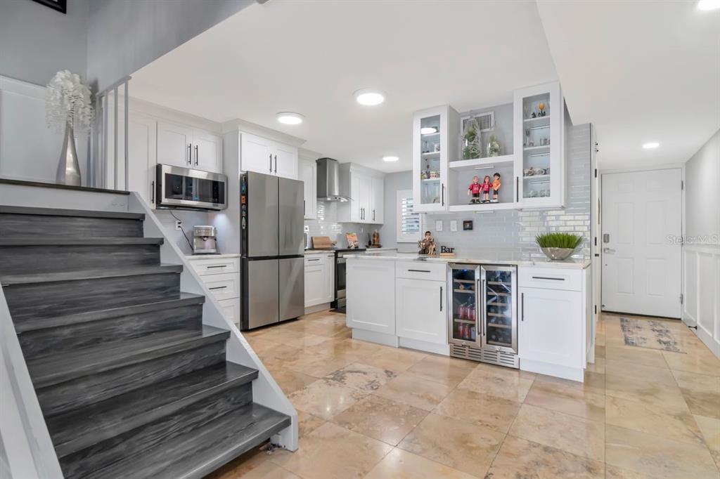 A kitchen with white cabinets, stainless steel appliances, a wine cooler, and dark wood stairs — 2424 W TAMPA BAY BOULEVARD UNIT C105, TAMPA, FL