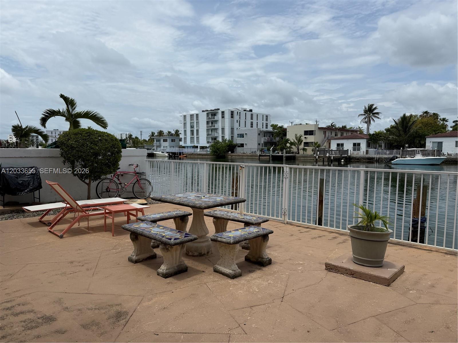 A patio with a stone table and benches overlooks a canal with boats and buildings — 8420 Byron Ave # 6, Miami Beach FL 33141, MIAMI BEACH, FL