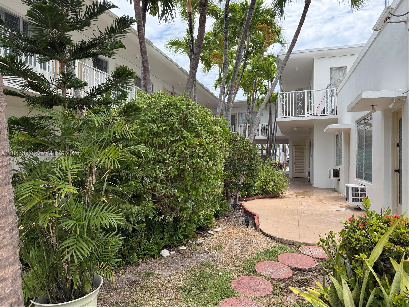 A courtyard with palm trees, landscaping, and a paved walkway between two-story apartment buildings — 8420 Byron Ave # 6, Miami Beach FL 33141, MIAMI BEACH, FL