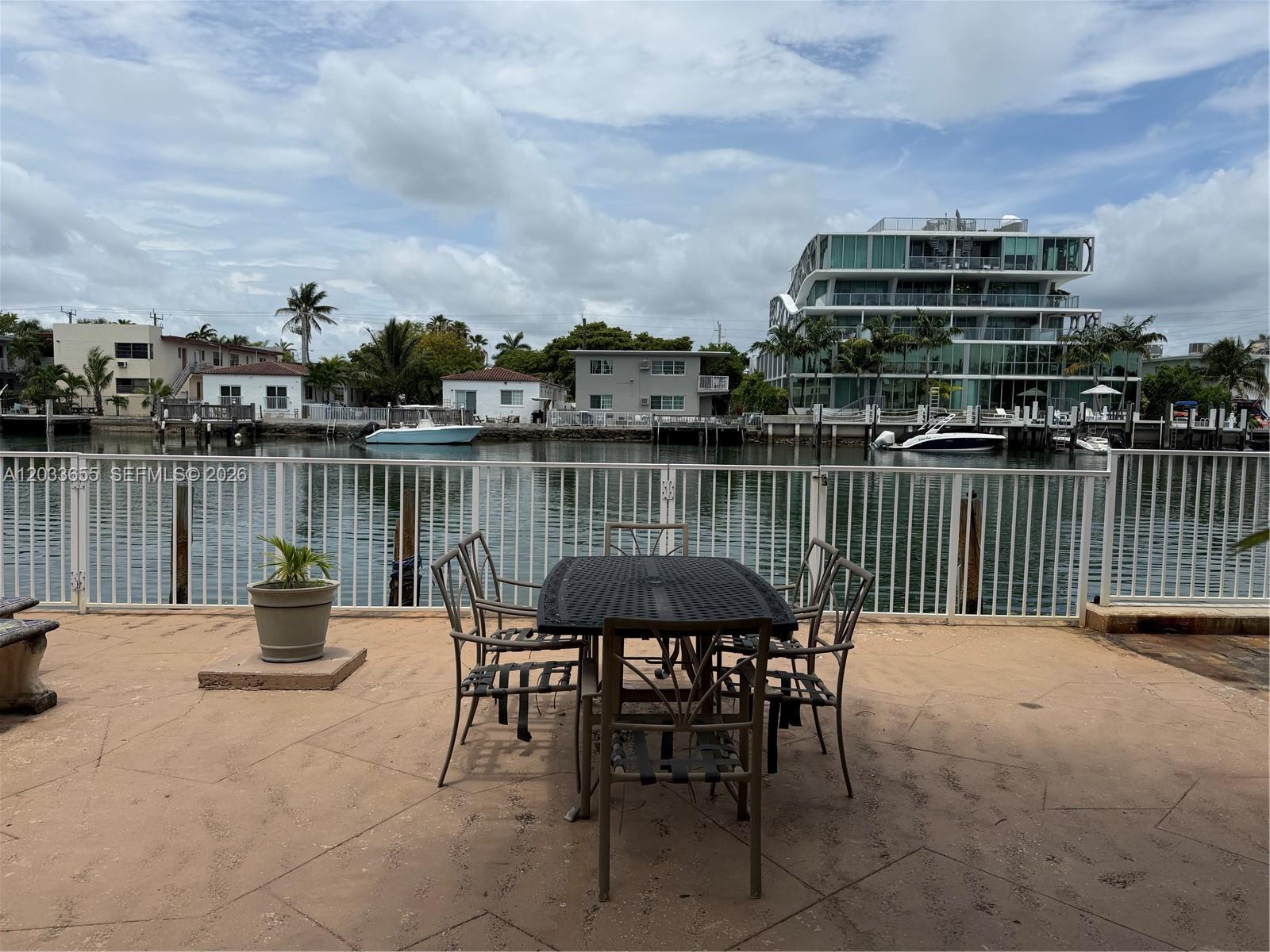 A patio with a metal dining set overlooks a canal with boats and nearby buildings — 8420 Byron Ave # 6, Miami Beach FL 33141, MIAMI BEACH, FL