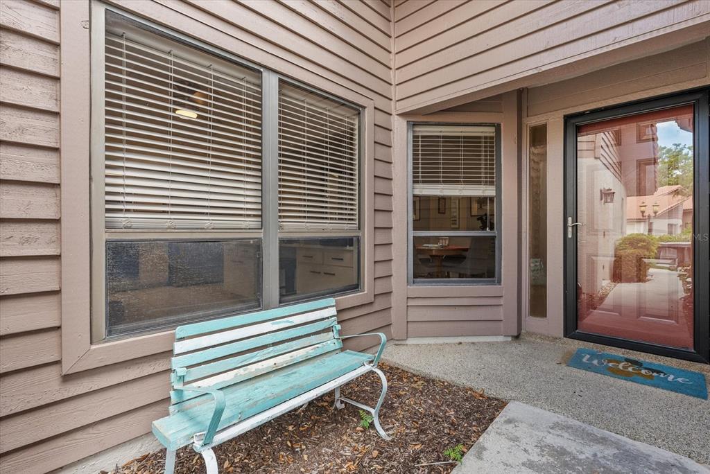A light blue wooden bench sits on a concrete porch outside a home's front entrance — 3862 WILSHIRE CIRCLE W UNIT 107, SARASOTA, FL