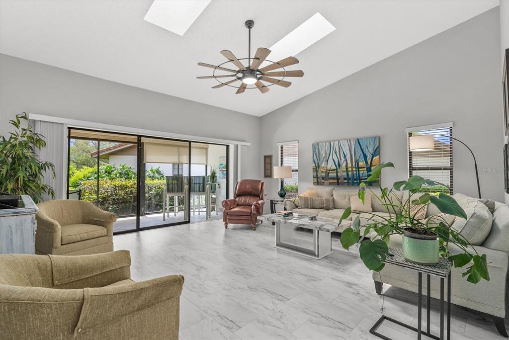 A living room features vaulted ceilings with skylights, a ceiling fan, and marble-look tile flooring — 3862 WILSHIRE CIRCLE W UNIT 107, SARASOTA, FL