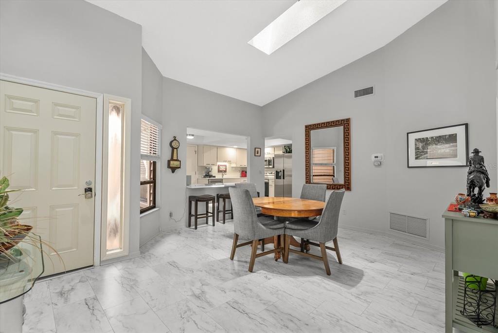 A dining area with a round table, gray chairs, and light marble-look tile flooring — 3862 WILSHIRE CIRCLE W UNIT 107, SARASOTA, FL
