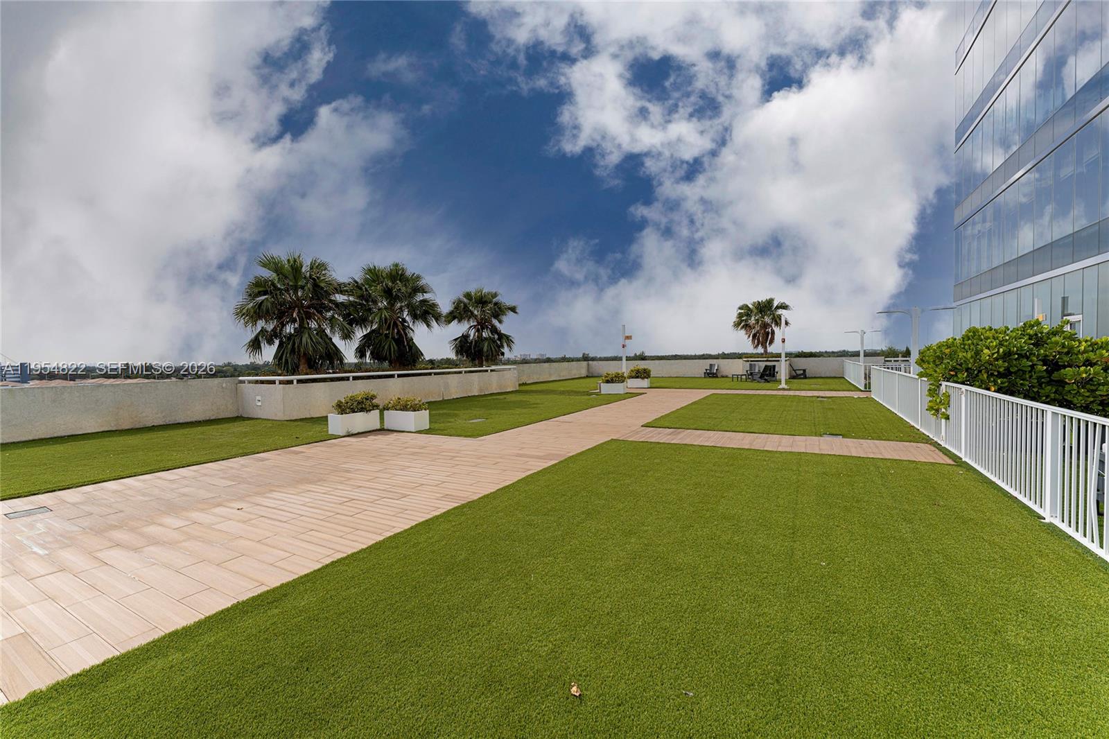 A rooftop terrace features artificial turf, paved walkways, palm trees, and a white railing — 20200 W Dixie Hwy # 903, Miami FL 33180, MIAMI, FL