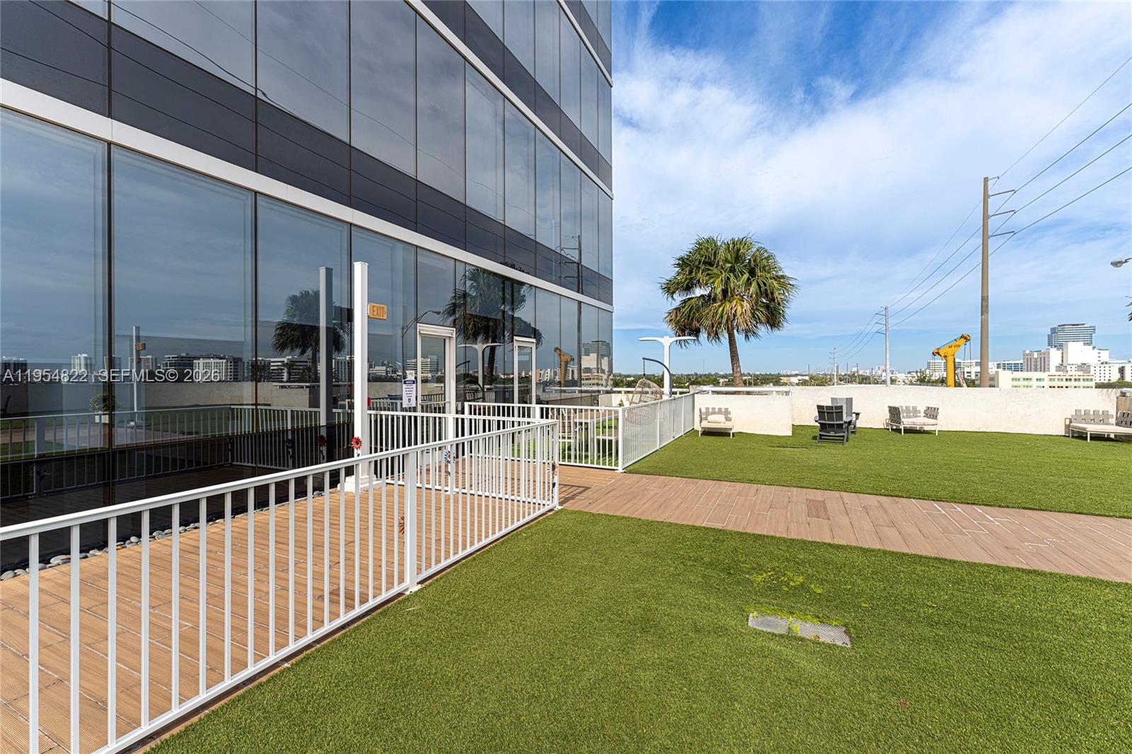 An outdoor terrace features artificial turf, a wooden walkway, white railings, and modern building glass — 20200 W Dixie Hwy # 903, Miami FL 33180, MIAMI, FL