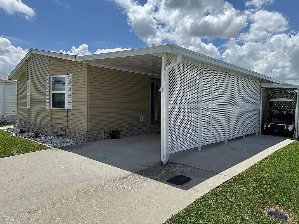 A tan mobile home features a concrete driveway, a covered carport, and white lattice screening — 57 STRAPHMORE DRIVE, HAINES CITY, FL