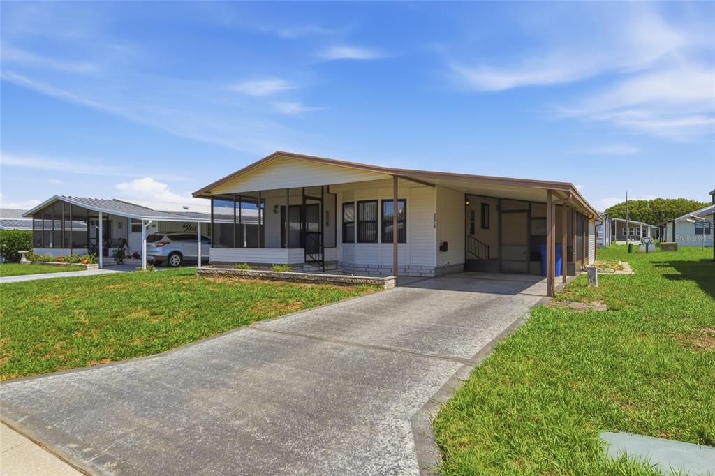 A single-story manufactured home with a concrete driveway, carport, and a screened-in front porch — 35919 VERANO LANE, ZEPHYRHILLS, FL