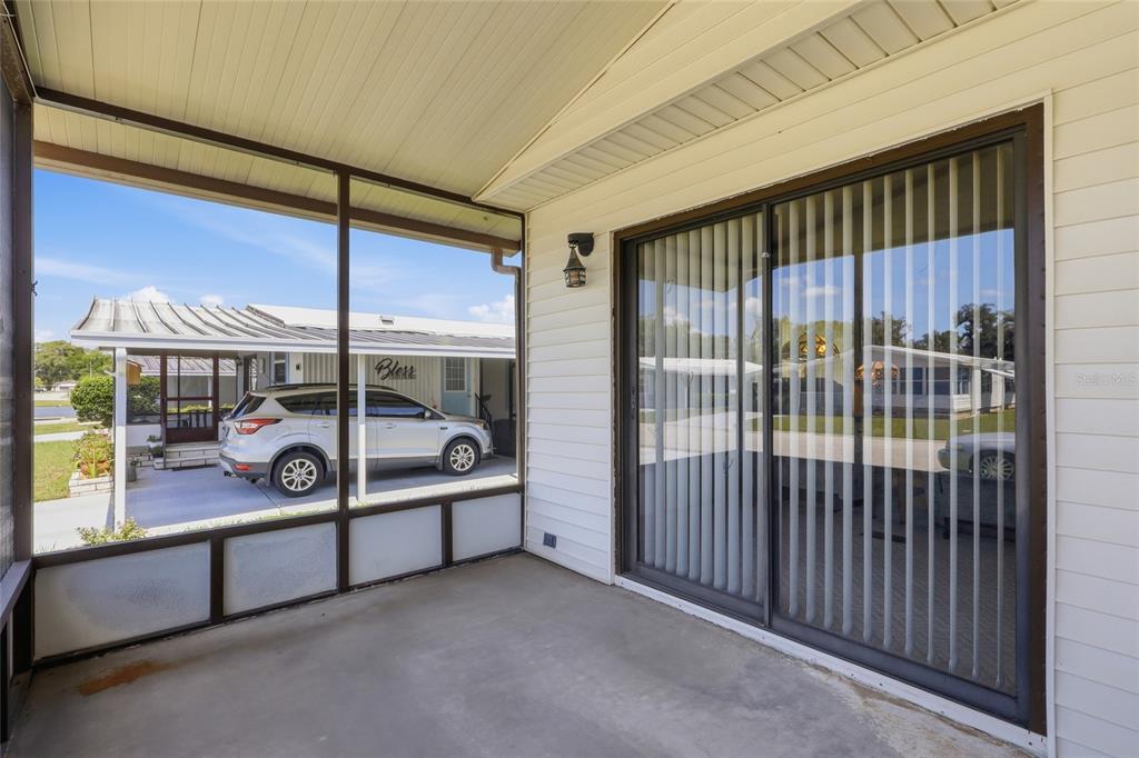 A covered screened-in porch with concrete flooring and a sliding glass door — 35919 VERANO LANE, ZEPHYRHILLS, FL