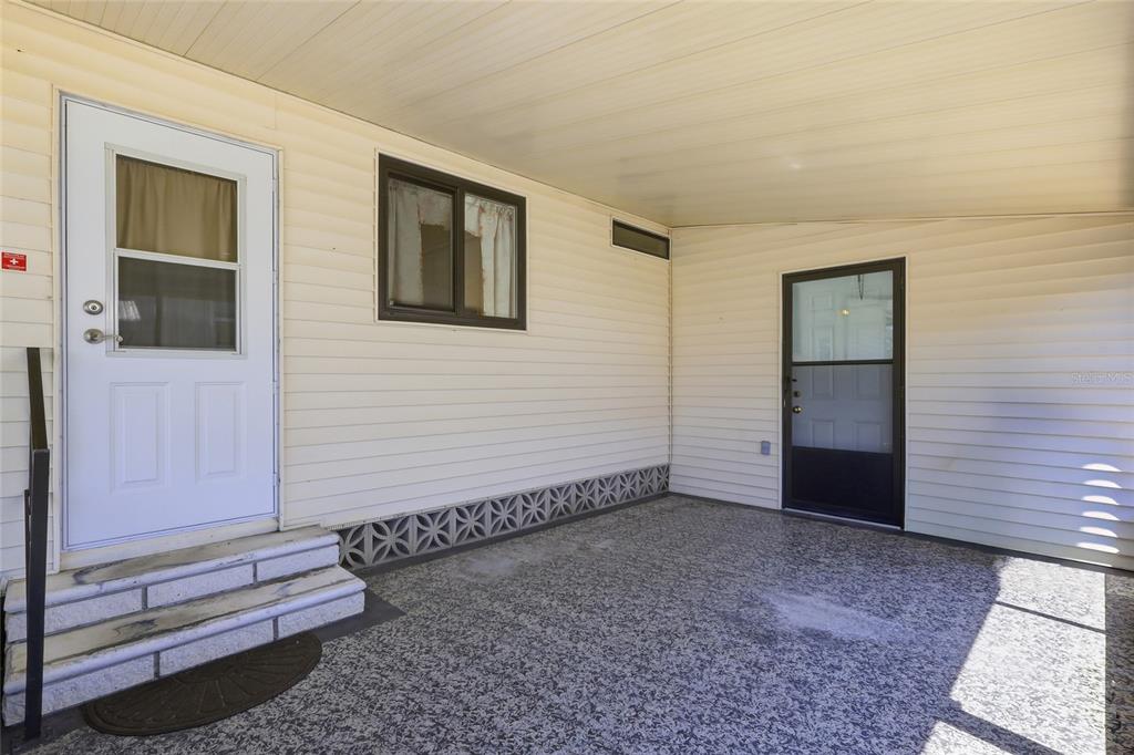 A covered patio features light-colored vinyl siding, a concrete floor, and two exterior doors — 35919 VERANO LANE, ZEPHYRHILLS, FL