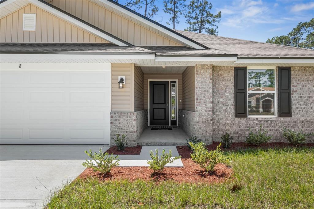 The exterior of a single-story house features a brick facade, tan siding, and a garage — 23 PRETORIA LANE, PALM COAST, FL
