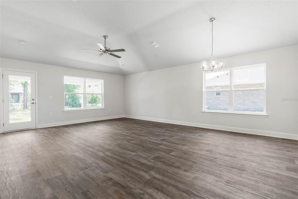 A spacious living room features light gray walls, dark wood-look flooring, and a vaulted ceiling — 23 PRETORIA LANE, PALM COAST, FL